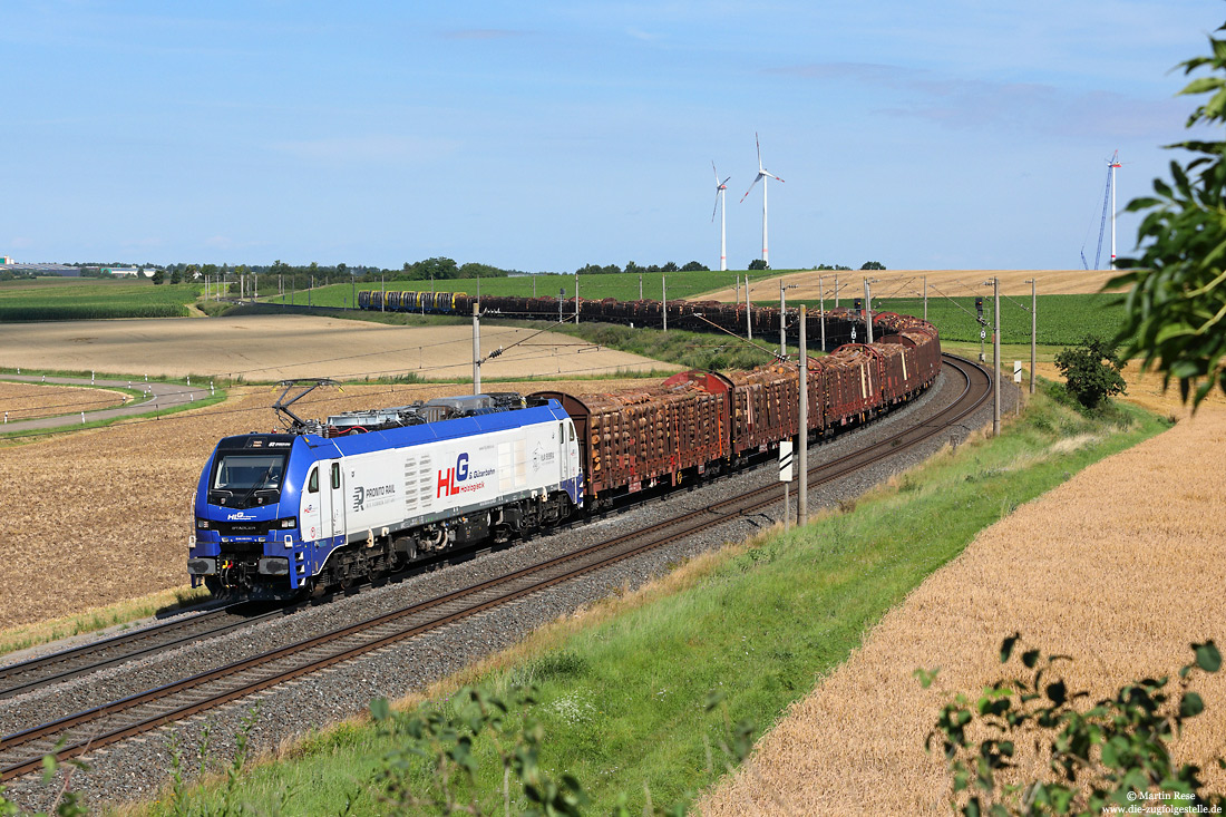 Die imposanten Zweikraftlokomotiven vom Typ Stadler Eurodual (Baureihe 159) erobern zunehmend die Strecken. Im Einsatz für das Unternehmen „Holzlogistik und Güterbahn GmbH“ zieht die 159 215 am 30.7.2021 einen langen Rohholzzug bei Herrnberchtheim gen Süden.