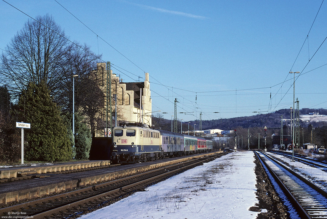 110 274 in ozeanblau/beige mit Eilzug im Bahnhof Schladern