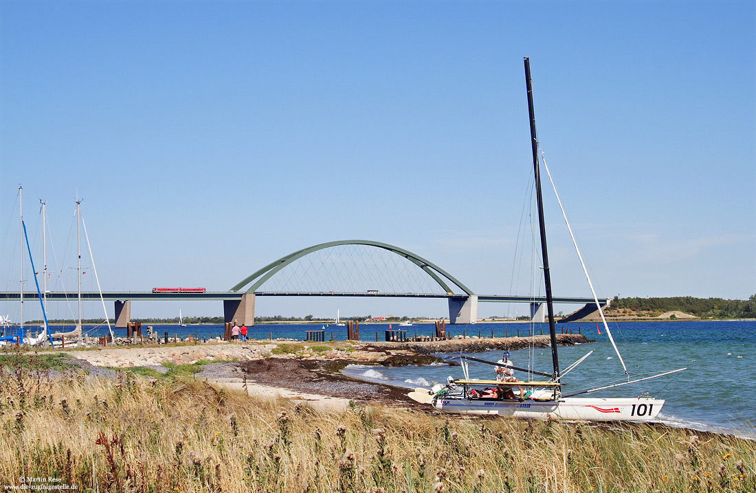 628 214 auf der Fehmarnsundbrücke mit Segelboot im Vordergrund