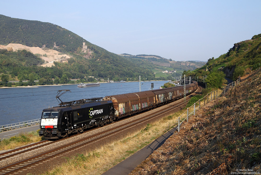 Am Morgen des 13.8.2015 rollt die Captrain-ES64 F4-111 mit einem Schiebewandwagenzug zwischen Lorch und Assmannshausen gen Süden. Auf der linken Rheinseite kann man die Burg Sooneck sowie dem Steinbruch der Hartsteinwerke Sooneck GmbH erkennen, wo jährlich mehrere hunderttausend Tonnen quarzitische Grauwacke gewonnen werden. 

